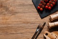 top view of fresh ripe tomatoes on slate board, fork with knife, seasonings in containers and peppercorns on wooden table