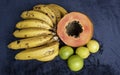 Top view of a fresh sliced orange papaya with seeds inside, a freckled bananas cluster and three green lemons over a blue navy and Royalty Free Stock Photo