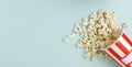 Top view of fresh spilled popcorn from the striped paper bowl on the bright blue background.Empty space for design Royalty Free Stock Photo