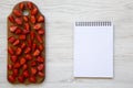 Top view, fresh strawberries on wooden board with blank notebook. Text area. White wooden table. From above Royalty Free Stock Photo