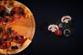 Top view of freshly baked pizza with salami olives peppers on a wooden tray on a black surface Royalty Free Stock Photo