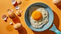 Top view of fried egg on a small frying pan near raw whole eggs and eggshells. Isolated on orange background with strong Royalty Free Stock Photo