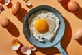 Top view of fried egg on a small frying pan near raw whole eggs and eggshells. Isolated on orange background with strong Royalty Free Stock Photo