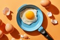 Top view of fried egg on a small frying pan near raw whole eggs and eggshells. Isolated on orange background with strong Royalty Free Stock Photo