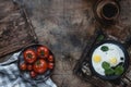 Top view of fried eggs with spinach on frying pan and tomatoes on plate