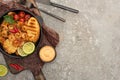 View of fried shrimps with grilled toasts, vegetables and lime served on board near cutlery and sauce on grey concrete