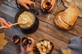 Top view friends cooking Swiss fondue assorted cheeses dinner on fire, hands holding mulled wine background wood board