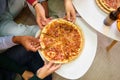 Top view of friends hands grabbing a pizza slice in a shared flat.