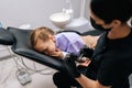 Closeup portrait of frightened cute little girl sitting in dental chair and looking at camera. Back view of female Royalty Free Stock Photo