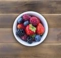 Top view. Fruits and berries in bowl on wooden background. Ripe raspberries, strawberries, blackberries and blueberries. Royalty Free Stock Photo