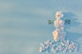 Top view on funny snowman made of white flowers petals on light blue background with sun shine. Holidays, winter