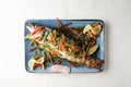 Top view of a garnished fish with vegetables on a blue plate