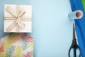 top view of gift box tied with bow and scissors with rolls of colorful paper on blue background with copy space