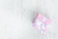 Top view of a gift box wrapped in pink dotted paper and tied satin bow over a white wood background.