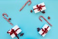 Top view on gift boxes wrapped white paper and red ribbon decorated berries, balls and candy canes on blue background. Flat lay. Royalty Free Stock Photo