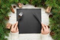Top view girl holds fork and knife in hand and is ready to eat. Empty black slate square plate on wooden christmas background. hol Royalty Free Stock Photo