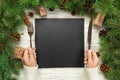 Top view girl holds fork and knife in hand and is ready to eat. Empty black slate square plate on wooden christmas background. hol Royalty Free Stock Photo