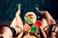 Top view. Girls in swimsuits eat fruits and drink cocktails drinks in swimming pool in summertime.
