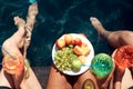 Top view. Girls in swimsuits eat fruits and drink cocktails in swimming pool in summertime.