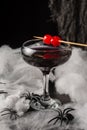 Top view of glass of black widow Halloween cocktail with red cherries and spiders on spider web, black background Royalty Free Stock Photo