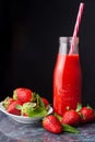 Top view of glass bottle with strawberry juice and striped straw, plate with strawberries, on blue marble, black background Royalty Free Stock Photo