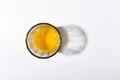 Top view of glass cup and fresh broken egg yolks in it on the white kitchen table.Empty space