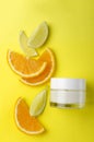 Top view of glass jar of moisturizing cream and pieces of citrus fruits on the yellow background