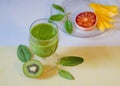 Top view of a glass of kiwi smoothie, half of a kiwi, green mint leaves and fruit slices in a plate