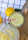 Top view of a glass with lemonade and lemon slice and a straw. Lemons, wooden table, towel, jug / pitcher on background Royalty Free Stock Photo