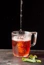 Top view of glass with rooibos tea falling on wooden table with mint leaves,