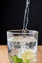 Top view of glass of water with falling water, mint, lemon and bubbles, vertically, on wooden table and black background, vertical