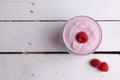 Top view of a glass of yogurt with raspberry on wooden background
