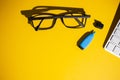 Top view of glasses, keyboard and a blue marker on a yellow work table Royalty Free Stock Photo