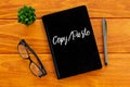 Top view of glasses,plant,pen and notebook written with Copy/Paste on wooden background.