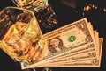 Top of view of glasses of whiskey near bottle on dollars money on a black table. Western theme style