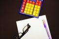 Top view of the glasses, on a white sheet. Black background. Bright colors calculator, purple pen and pencil. Business Royalty Free Stock Photo