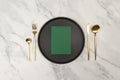 Top view of gold cutlery and black plate on white marble background. Table setting menu, empty paper blank flat lay.