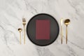 Top view of gold cutlery and black plate on white marble background. Table setting menu, empty paper blank flat lay.