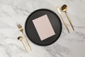 Top view of gold cutlery and black plate on white marble background. Table setting menu, empty paper blank flat lay.