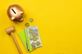 Top view of a piggy bank, coins, banknote, notebook, hammer on a yellow surface with copy space