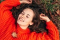 Top view of a gorgeous young woman smiling and wearing orange knitted sweater posing on the grass with autumn leaves. Beautiful Royalty Free Stock Photo