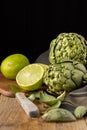 Top view of green artichokes with black cloth, limes on table and knife, on wooden table, with selective focus, black background Royalty Free Stock Photo