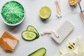 Top view of green bath salts, soap and pumice stone near fresh flower, lime and cucumber on marble surface.