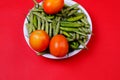 Top view of green beans, chili pepper, and tomatoes on plate isolated on red background Royalty Free Stock Photo