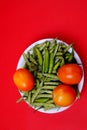 Top view of green beans, chili pepper, and tomatoes on plate isolated on red background Royalty Free Stock Photo