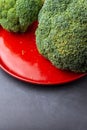 Top view of green broccoli on red plate and dark surface in vertical, with selective focus Royalty Free Stock Photo