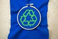 Top view of green embroidered sign of recycling on blue fabric in a hoop