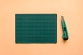 Top view of green rubber cutting mat with green cutter over pale orange color paper background. Background with copy space Royalty Free Stock Photo
