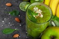 A top view of a green smoothie with kiwi and grated almonds on a dark gray background. Tropical fruits on a desk.