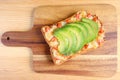 Top view of a grilled cheese toast with tomato and sliced fresh ripe avocado on wooden breadboard Royalty Free Stock Photo